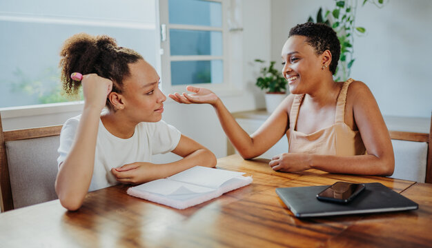 Happy African American mother helping her teenage daughter with school homework at home.