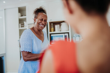Fototapeta premium Happy senior Black woman laughing while talking to a friend in a modern kitchen at home.
