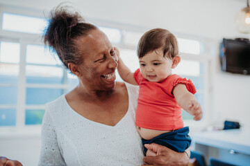 Happy African American grandmother holding her adorable toddler granddaughter at home