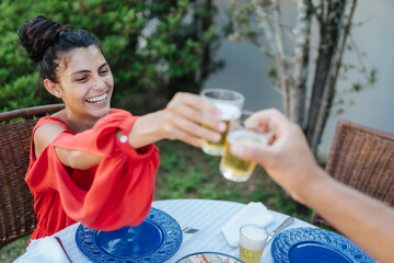 Happy young woman clinking glasses of beer with a friend at an outdoor garden party.