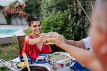 Happy young woman clinking glasses during an outdoor lunch with family in a backyard garden.
