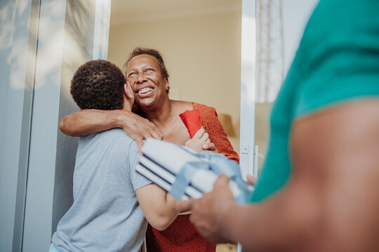Happy African American grandmother hugging her grandson at the front door while receiving a gift from family.
