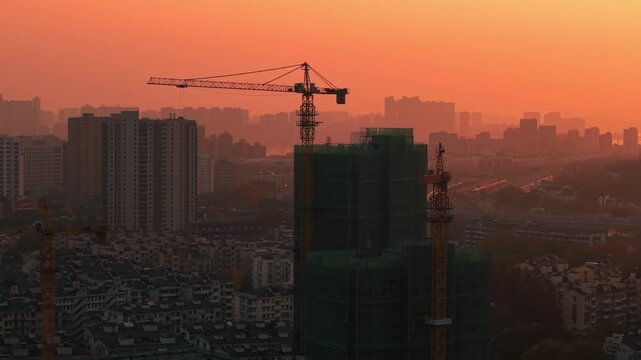 Orange sky over construction site during sunset, buildings under construction with cranes in the evening