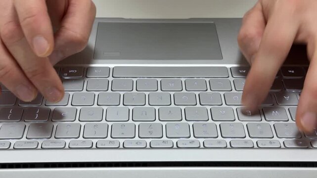 Person types on the keyboard of a silver laptop in a studio setting during the day.