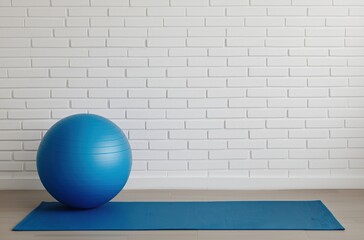 Blue exercise ball and yoga mat on a wooden floor in front of a white brick wall, ready for a workout