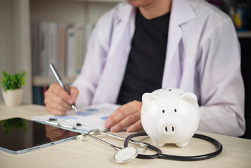 Doctor with stethoscope and white piggy bank on desk, concepts of healthcare costs, medical insurance planning, and saving money for health treatment expenses.