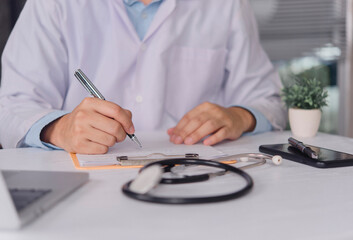 Close up doctor hand writing prescription on clipboard with stethoscope on desk. Professional physician filling medical report and insurance form in hospital clinic. Healthcare administrative concept.
