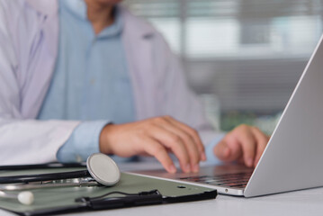 Doctor typing on laptop computer with stethoscope on clipboard at desk. Medicine doctor working on medical report and telemedicine concept.