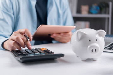 Man using calculator and holding digital tablet for financial planning. Budgeting, tax return calculation and savings concept with white piggy bank on desk.