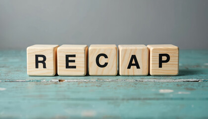 Wooden cubes spell out RECAP on a distressed wooden table surface. Simple, clean presentation conveys the idea of summary or final review. Conceptual still life.