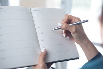 Business woman planning work event, hand writing on weekly schedule notebook, close up. Business event planning, timetable agenda plan