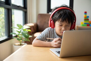 Focused asian boy wearing red headphones studying online with a laptop and holding a wooden pencil