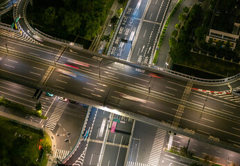 Aerial view of a busy highway intersection at night in an urban area, with moving car light trails. © Evgenii Bakhchev