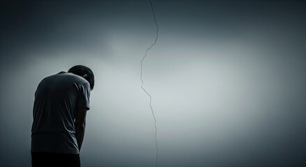 A man standing in front of a cracked wall with his head bowed, possibly in distress.