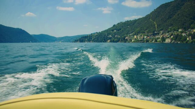 Boat moving across Lake Como leaving wake trails on the water with mountain scenery.