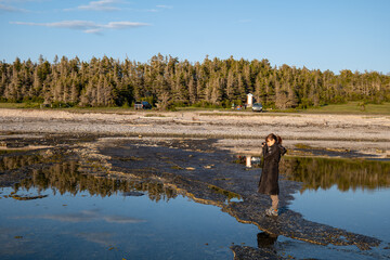 A Peruvian Woman Takes Photos with a Camera and Strolls through Baie Sainte-Claire at the Sunset, in Anticosti, Quebec, Canada