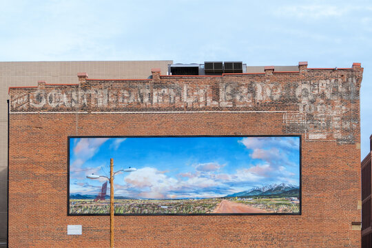 mural at an old brick wall with historic advertising and wooden pylon in front with painting from Don Stinson