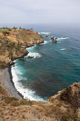 Fototapeta premium High viewpoint of rugged cliffs, turquoise Atlantic surf, and offshore rocks along steep coastline under hazy sky at Rambla de Castro, Tenerife, Canary Islands, Spain.