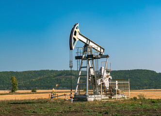 A large oil pump jack operates in an open field, extracting crude oil
