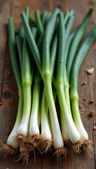 Fototapeta premium Fresh green onions bunch with roots sit on rustic wooden table. Green stalks and white bases show off their natural freshness. Healthy ingredient for cooking meals.
