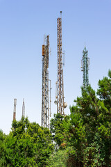 Cell phone towers with antennas above green trees, telecommunications infrastructure against clear blue sky.