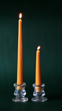 Two yellow beeswax candles burning against a green background in glass candlestick holders