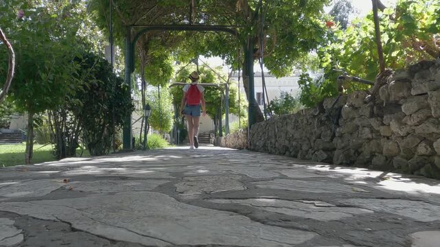 Traveler tourist woman with hat and red backpack explore the gardens of Achillion palace on Corfu island, Greece, slow motion