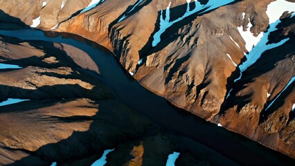 Aerial view of a winding river cutting through rugged mountain terrain with patches of snow