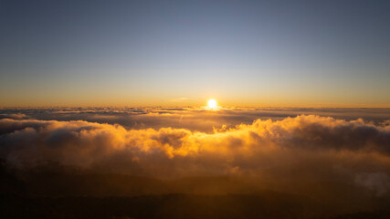 Natural view Golden sunrise above a sea of clouds, with warm light illuminating misty layers beneath a clear morning sky.