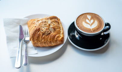 A perfect morning starts with a beautifully crafted latte and a flaky almond croissant on a minimalist white table