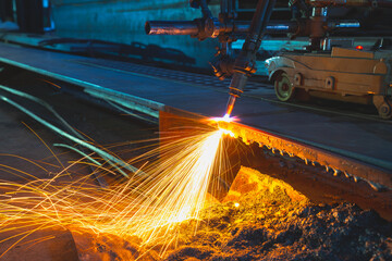 Acetylene torch semi auto machine cutting metalwork fabrication with bright sparks in factory.