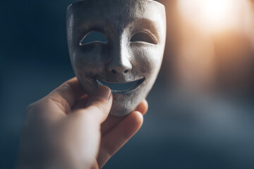 Close-up of a human hand holding a smiling theatrical mask symbolizing hidden sadness and emotional duality