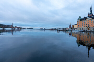 Obraz premium Calm winter reflections across the waterfront in Stockholm, Sweden, with the historic skyline of Gamla Stan and the soaring spire of Riddarholmen Church mirrored on the glassy harbor.
