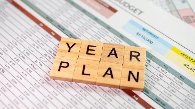 year plan wooden blocks on financial spreadsheet, business budget and profit loss documents, office desk close up