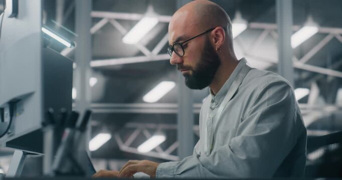 Bearded Male IT Specialist With Glasses, Intensely Focused on Computer Monitor. Background Features Cool, Technical Environment of Server Control Room. Critical Data Analysis and Dedicated Expertise.