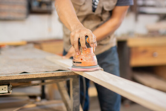 Close-up of a man using a hand sander. Carpenter sanding wood on a workbench