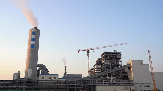 Industrial plant with smoking chimney and ongoing construction of factory buildings