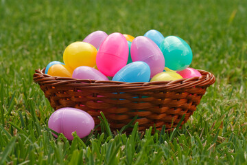 Wooden basket filled with Easter eggs on grass with a single purple egg laying outside