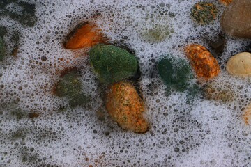 Background, texture of sea pebbles in the sea foam of the surf