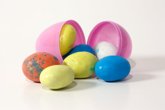 Pink plastic Easter egg filled with some chocolate eggs against a white background