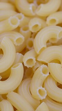 Bulk uncooked macaroni heap suggests wholesale stock factory packaging, dense pile conveys volume and commerce, neutral tones suitable for food industry or supply chain visuals