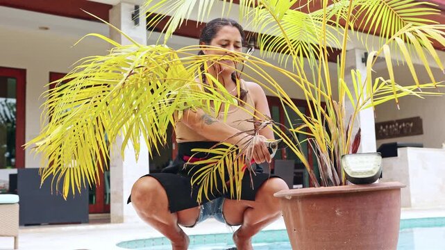 Mature woman pruning a yellow palm plant in her backyard