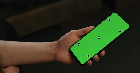 young woman lying on a couch and holding smartphone with vertical green screen