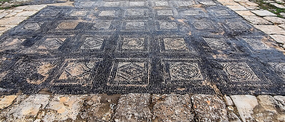 Aged mosaic floor with repeating geometric patterns: dark tiles form the background, highlighting lighter squares, diamonds, and spirals
