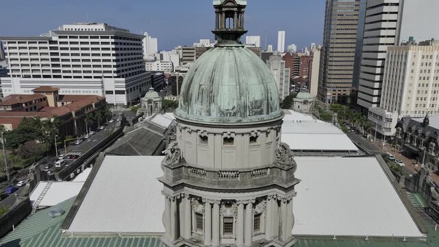 Drone flies to the right in medium shot of main tower at city hall on sunny day in downtown Durban, South Africa