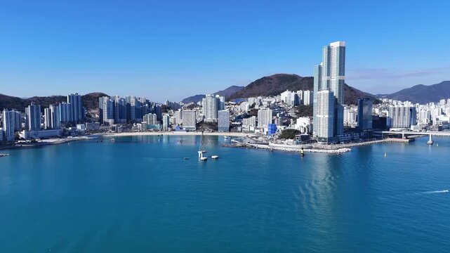 Drone footage captured during daytime flying toward coastal city over turquoise sea under clear weather conditions. Aerial wide shot suitable for travel tourism real estate urban lifestyle and backgro