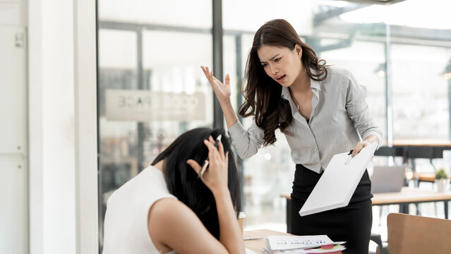 Angry female boss shouting at stressed employee in office. Conflict, work pressure, and toxic workplace environment between colleagues.