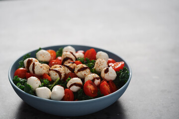 Salad with mozzarella, tomatoes and kale leaves in blue bowl on concrete countertop