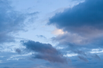 Obraz premium Layered blue and lavender clouds drift across a tranquil evening sky, with soft gradients and gentle light creating a calm, atmospheric scene.