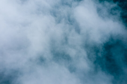 Billowing white clouds drift over a blue background, creating an abstract, minimal composition with gentle gradients and soft textures. The image evokes a tranquil, airy mood and a sense of calm